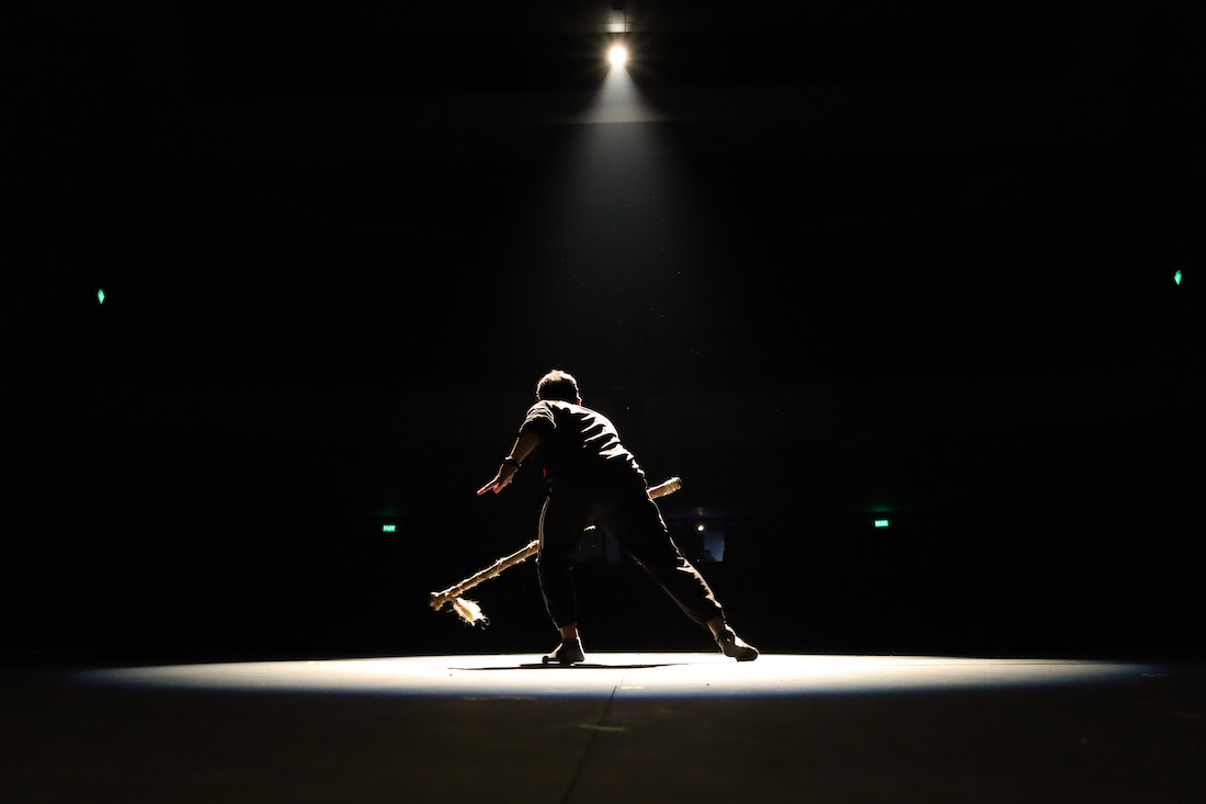 Artista de espaldas en escenario con fondo negro con luz focal