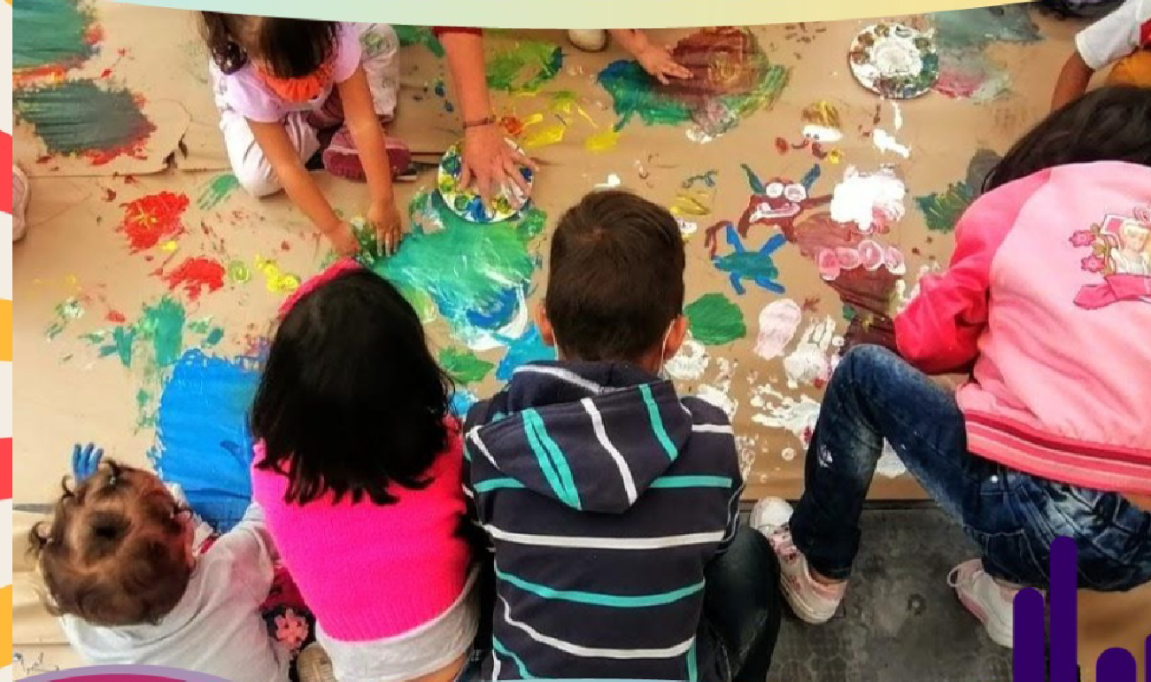 Grupo de niños y niñas de diferentes edades jugando con pintura sobre papel craft.