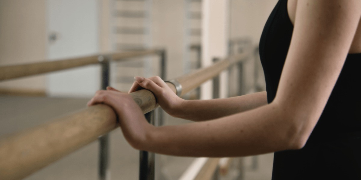 Mujer apoyada en barra de ballet.
