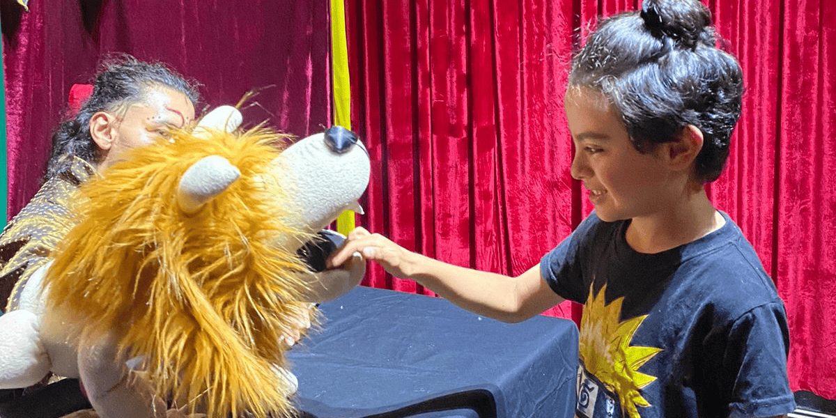 Fotografía de una obra de títeres con un león y un niño presente