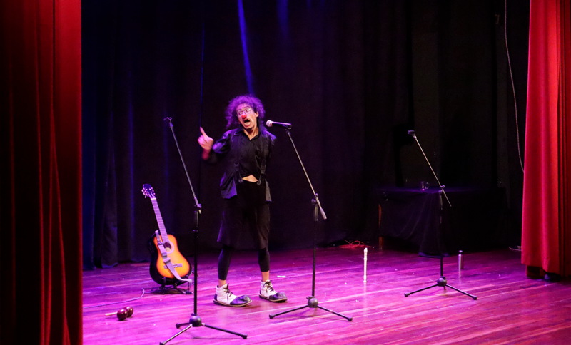 Hombre actuando en un escenario con una guitarra al lado