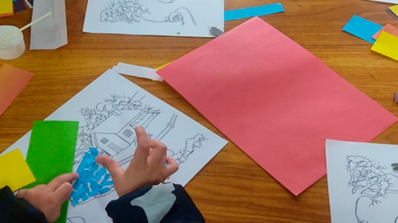 manos de niño cortando papeles de colores sobre una mesa