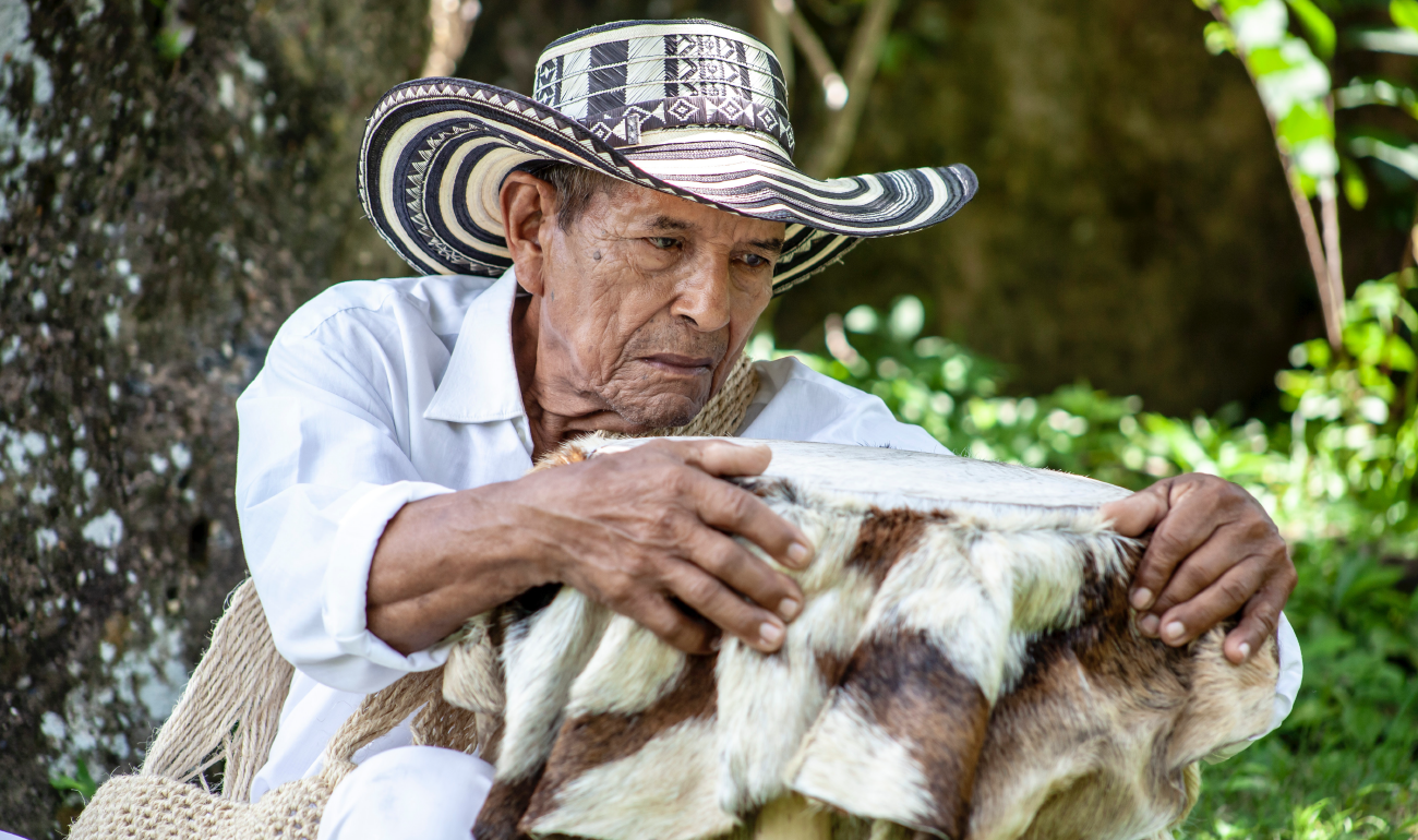 Hombre mayor armando una tambora. Cuenta con una camisa blanca y un sombrero vueltiado.