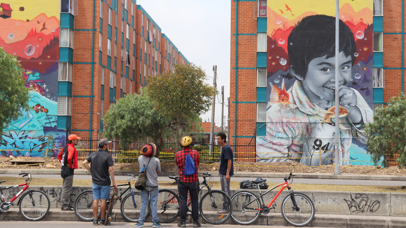 personas en bicicleta observando un grafiti en una fachada
