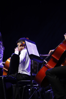 Niño de orquesta sinfónica ejecuta violonchelo, lee partitura