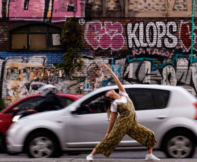 mujer estirando y dos carros de fondo pasando detrás