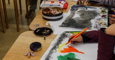 Fotografía de una mesa con implementos de dibujo y niños pintando