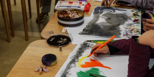 Fotografía de una mesa con implementos de dibujo y niños pintando